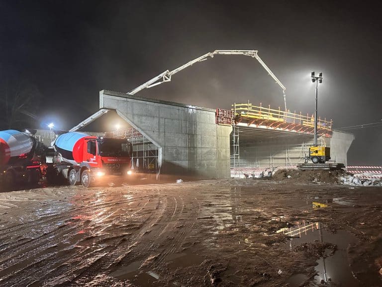 Budowa mostu na drodze w nocy, z ciężkim sprzętem i mokrą, błotnistą nawierzchnią.