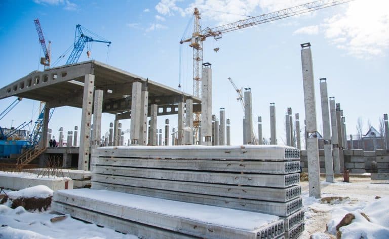 Budowa nowego obiektu na placu budowy z żelbetowymi słupami i dźwigami, w tle niebo z chmurami.