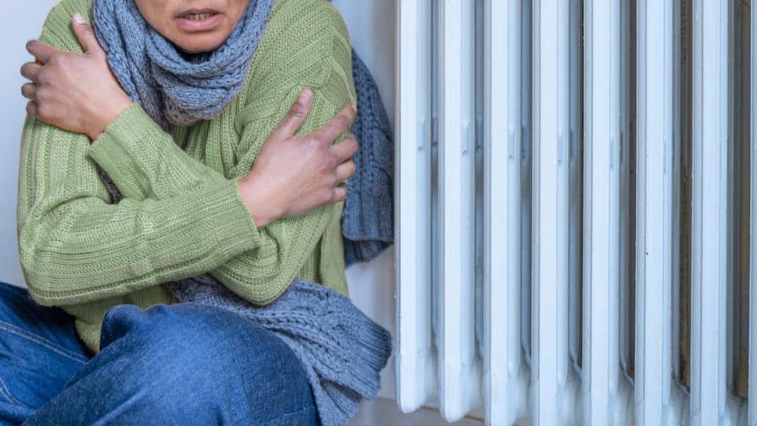 Kobieta trzyma się za klatkę piersiową przy grzejniku, wyraz b&oacute;lu lub dyskomfortu na twarzy.