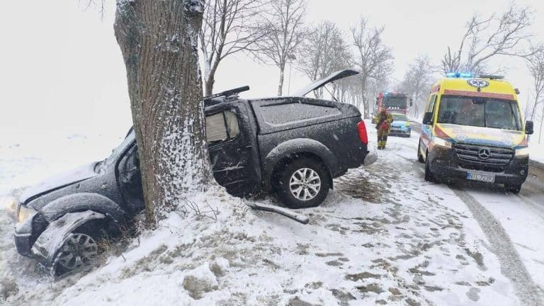 Rozbity Nissan Navara po wypadku na śliskiej drodze, uderzony w drzewo, na miejscu służby ratunkowe.