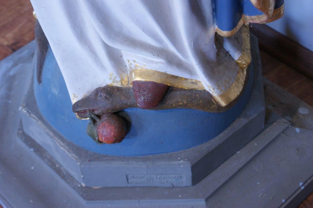 Detaliczny widok na podstawę figury Matki Bożej w Gietrzwałdzie, z widocznymi śladami zmian w malowaniu i dekoracji.