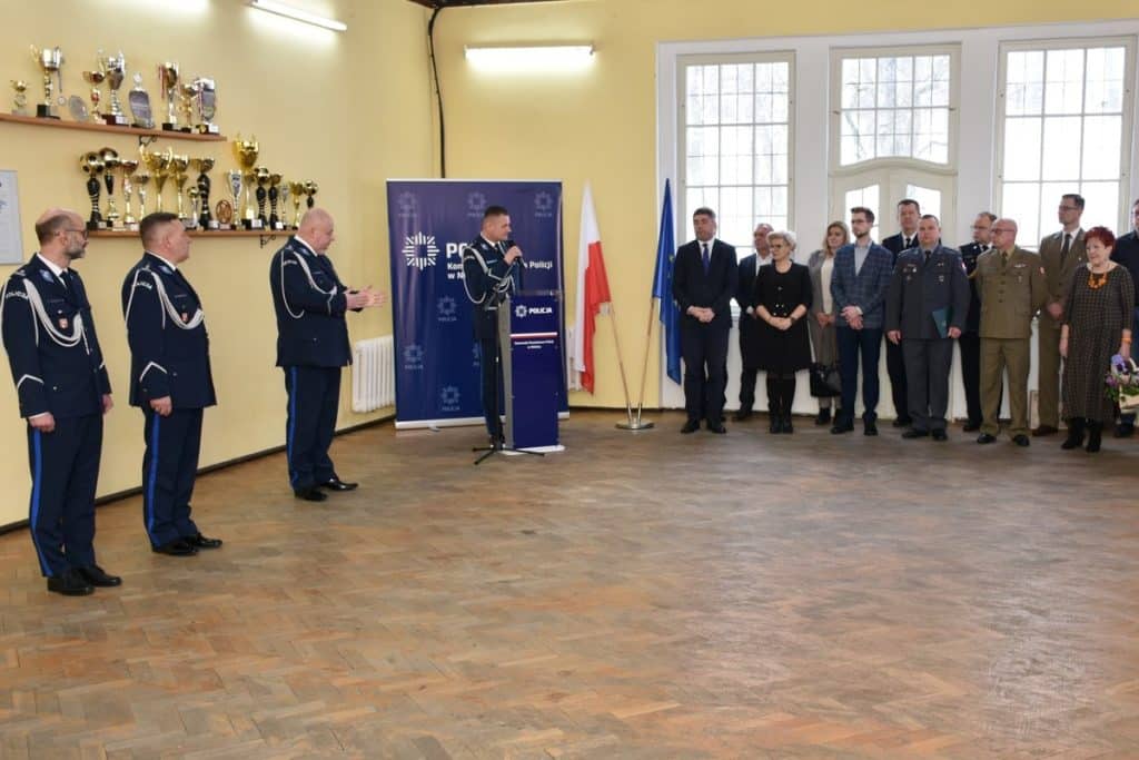 Sala w komendzie policji z grupą funkcjonariuszy i gości podczas uroczystości.