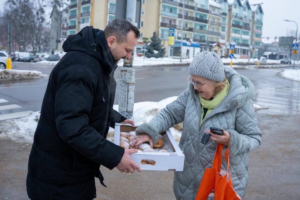 Prezydent Olsztyna rozdaje pączki na ulicy, uśmiechając się do mieszkańc&oacute;w.