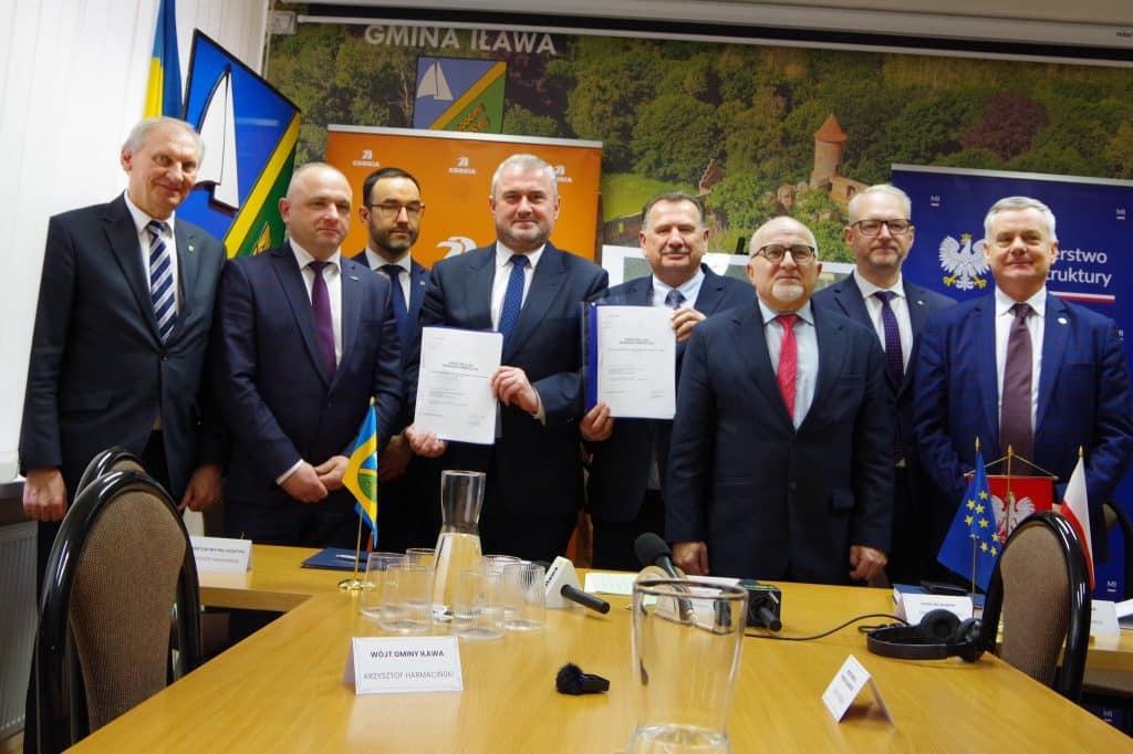 Grupa mężczyzn w formalnych ubraniach podczas podpisania umowy na budowę wiaduktu na DK16 w Iławie.