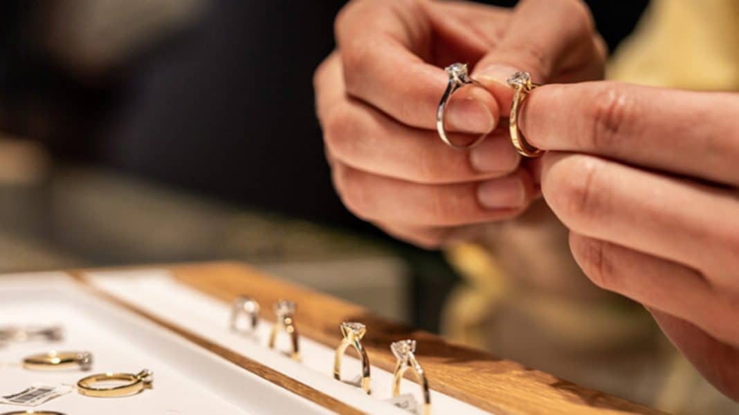 Osoba trzyma dwie obrączki złote i srebrne, na tle innych biżuterii na stole.