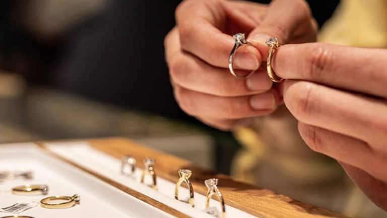 Osoba trzyma dwie obrączki złote i srebrne, na tle innych biżuterii na stole.