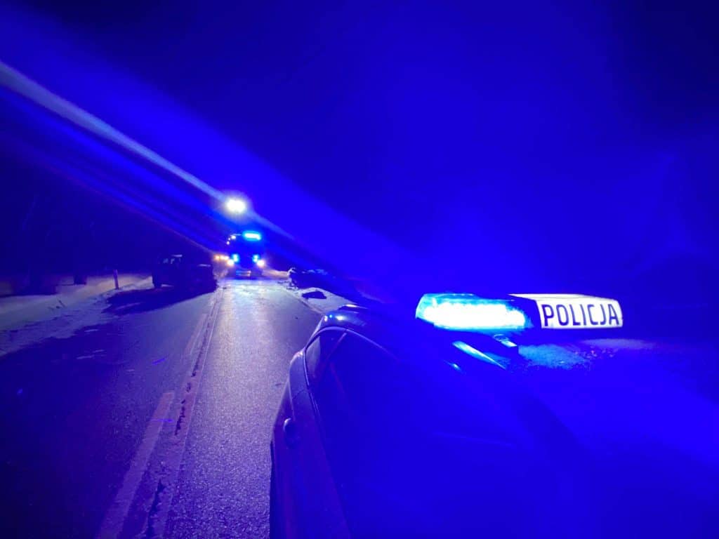 Policja na miejscu wypadku na drodze krajowej, samochody z uszkodzeniami, nocne warunki.