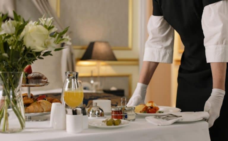 St&oacute;ł śniadaniowy z kwiatami, napojami i jedzeniem, w tle lampa i eleganckie wnętrze.