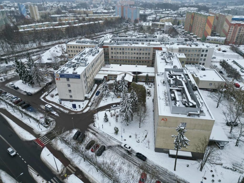 Widok na szpital dziecięcy w Olsztynie pokryty śniegiem, z dużym budynkiem i otaczającymi go drzewami.