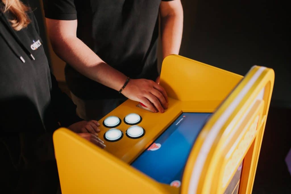 Osoba grająca na automacie do gier w centrum miasta, widoczne ręce i część urządzenia.