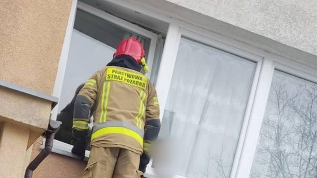 Strażak otwiera okno w mieszkaniu na trzecim piętrze, ratując roczne dziecko zamknięte w środku.