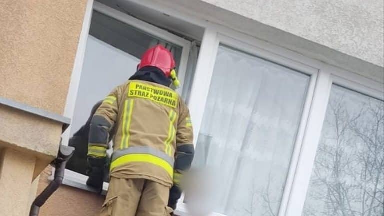 Strażak otwiera okno w mieszkaniu na trzecim piętrze, ratując roczne dziecko zamknięte w środku.