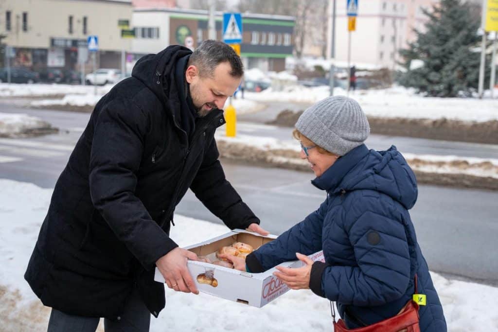 Prezydent Olsztyna rozdaje pączki mieszkańcom na ulicy w zimowej scenerii.