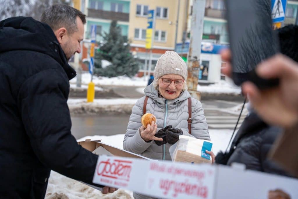 Prezydent Olsztyna rozdaje pączki mieszkańcom na ulicy w zimowej scenerii.