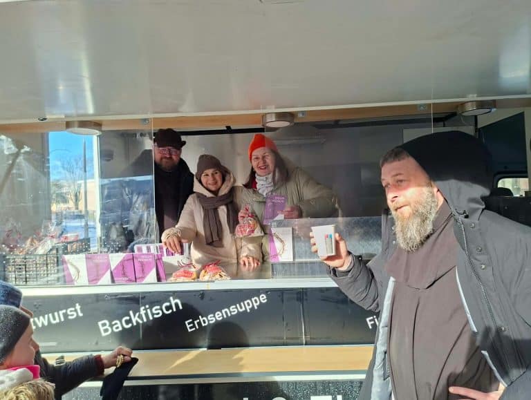 Grupa ludzi w food trucku na ulicy, uśmiechnięci i rozmawiający, w tle widoczne zimowe otoczenie.