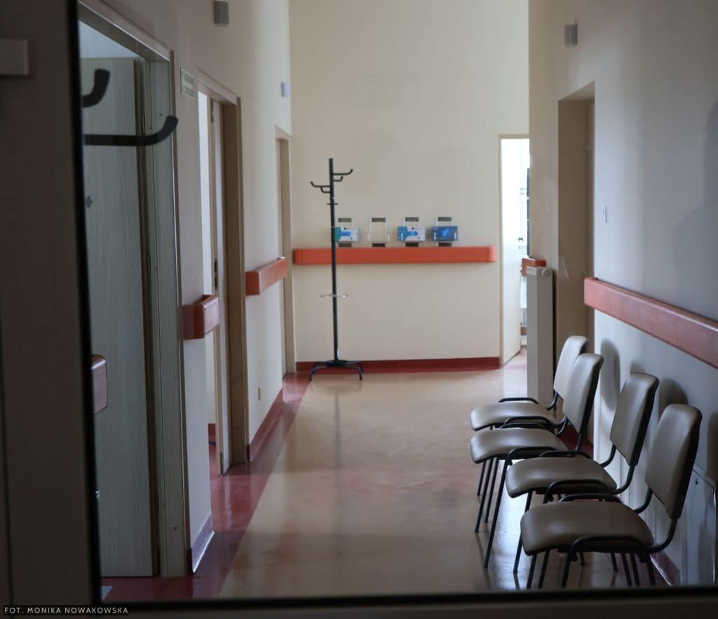 Widok na korytarz w nowo wybudowanym ośrodku rehabilitacyjnym z krzesłami i w&oacute;zkiem na ubrania.