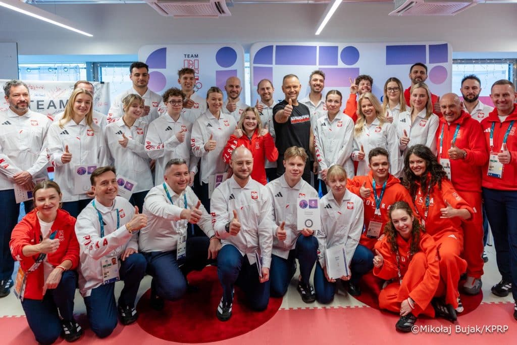 Grupa ludzi w sportowych strojach, niekt&oacute;rzy uśmiechają się i pokazują kciuki w g&oacute;rę.