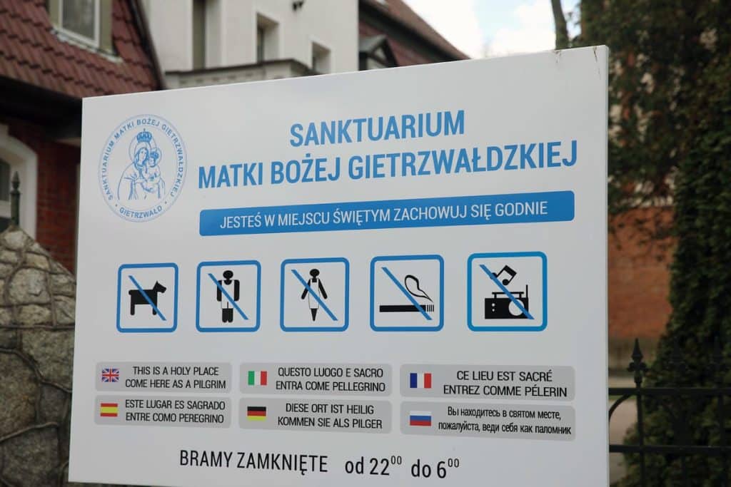 Tablica informacyjna przy sanktuarium w Gietrzwałdzie z zakazami i prośbą o zachowanie się godnie.