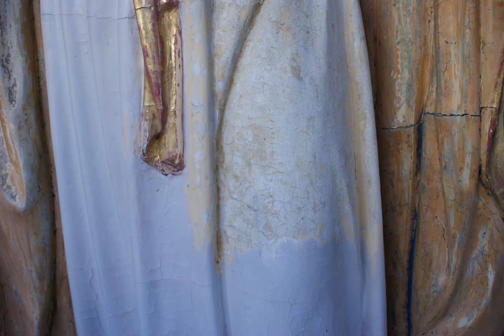 Zbliżenie na fragment figury Matki Bożej, ukazujący zmiany w jej wyglądzie i uszkodzenia powierzchni.