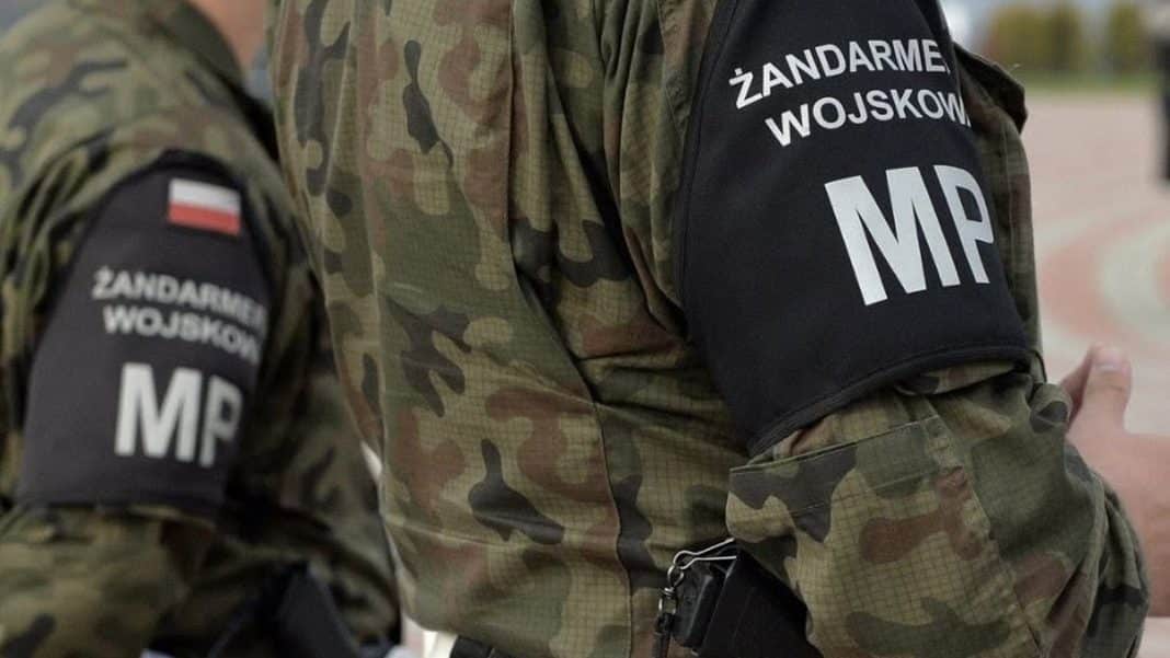 Żołnierze w mundurach wojskowych z napisem Żandarmeria Wojskowa na ramionach, na tle nieznanego otoczenia.