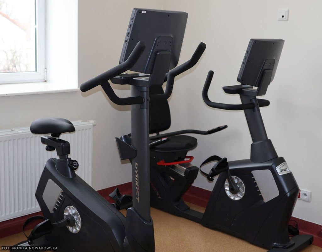 Wewnątrz nowoczesnej sali rehabilitacyjnej z dwoma rowerami stacjonarnymi.