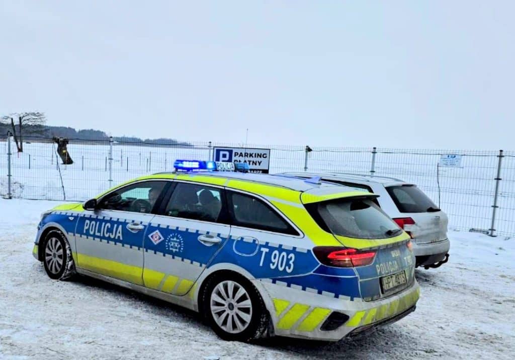 Policja na zamarzniętym jeziorze podczas kontroli, w tle zamarznięte jezioro i ogrodzenie.