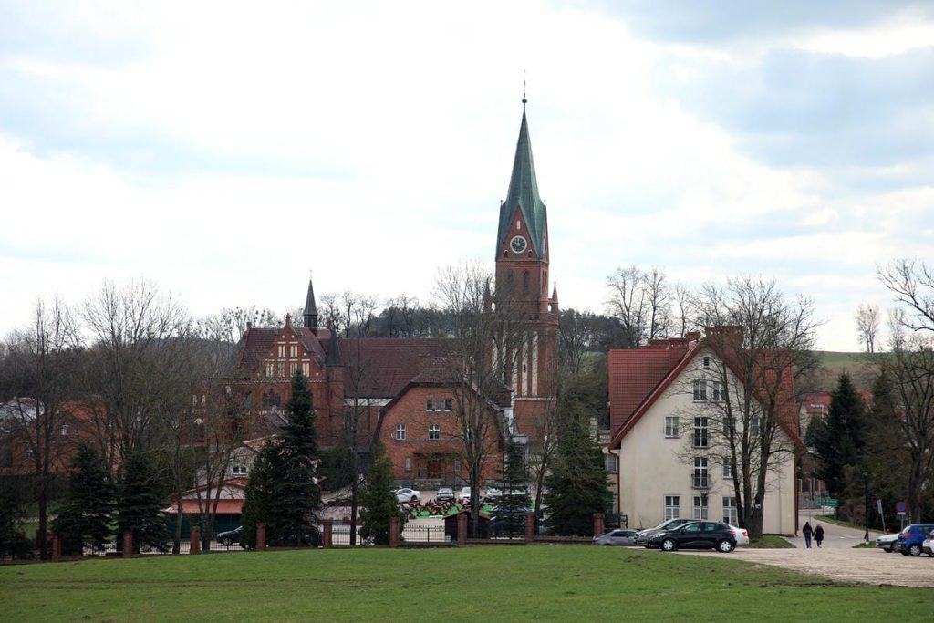 Widok na zabytkową bazylikę w Gietrzwałdzie z pękającymi ścianami i otaczającymi budynkami.