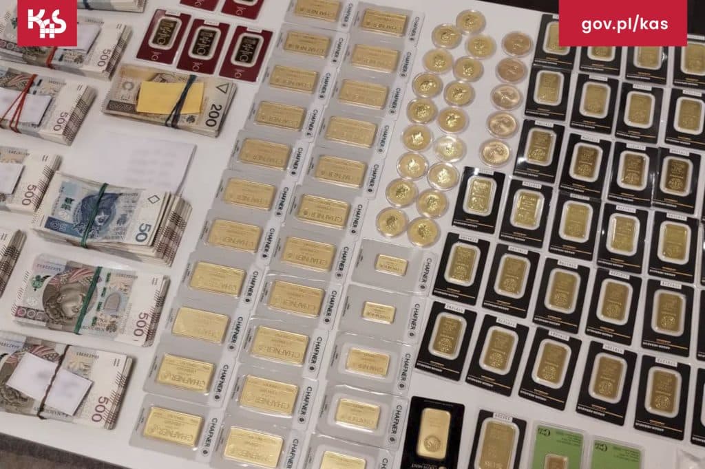 Na zdjęciu widoczne są złote sztabki, monety, banknoty i inne przedmioty związane z handlem pieniędzmi.