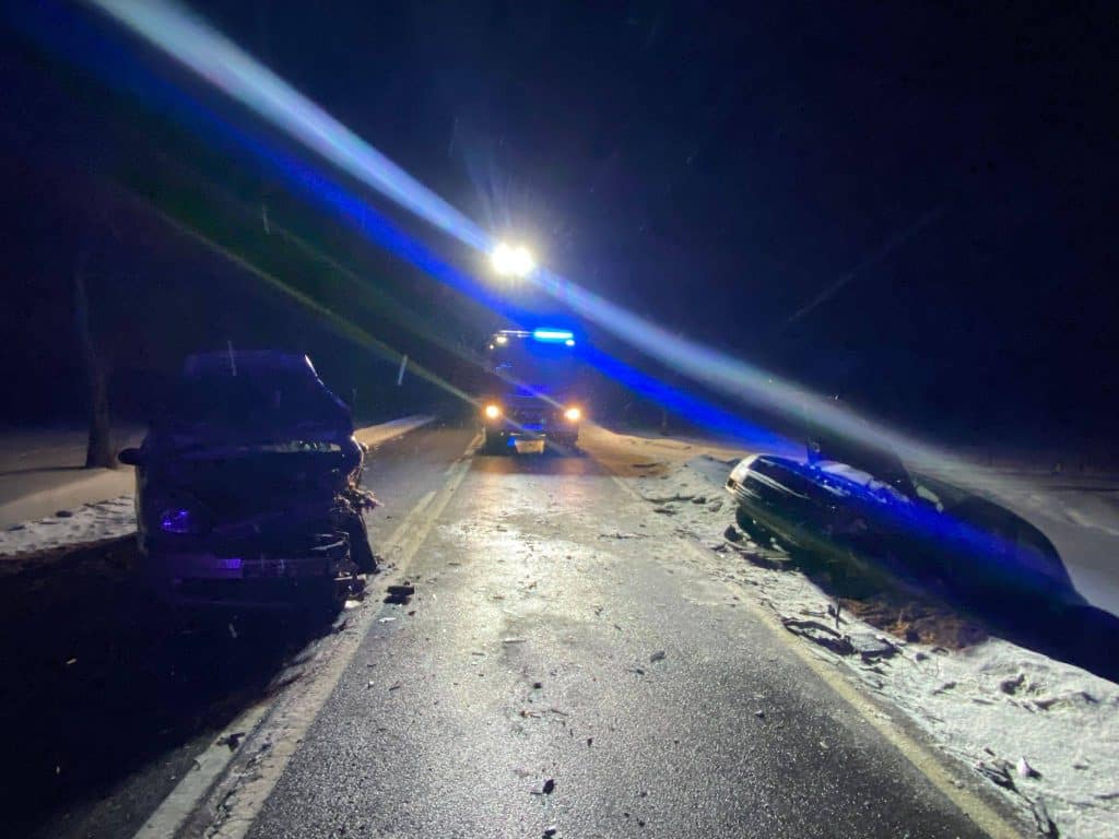 Wypadek trzech samochod&oacute;w na drodze krajowej w nocy, uszkodzone pojazdy na jezdni, służby na miejscu.