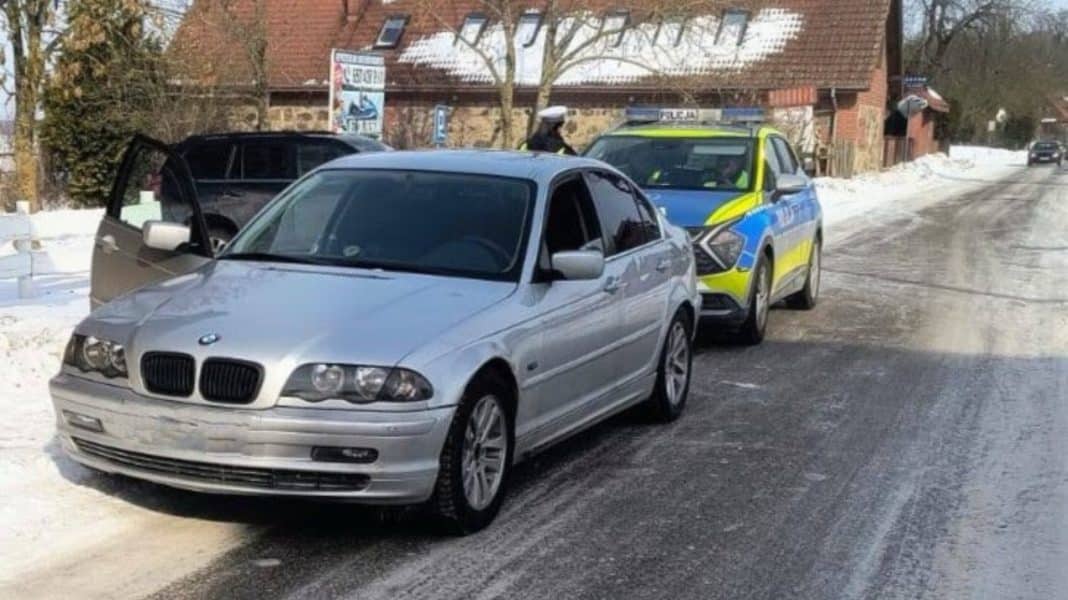 Samoch&oacute;d zatrzymany na zimowej drodze z policyjnym radiowozem w tle.