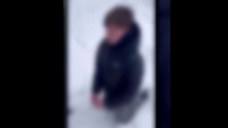 Zamazany, nieostry obraz chłopca klęczącego na śniegu, ubrany w ciemną kurtkę.