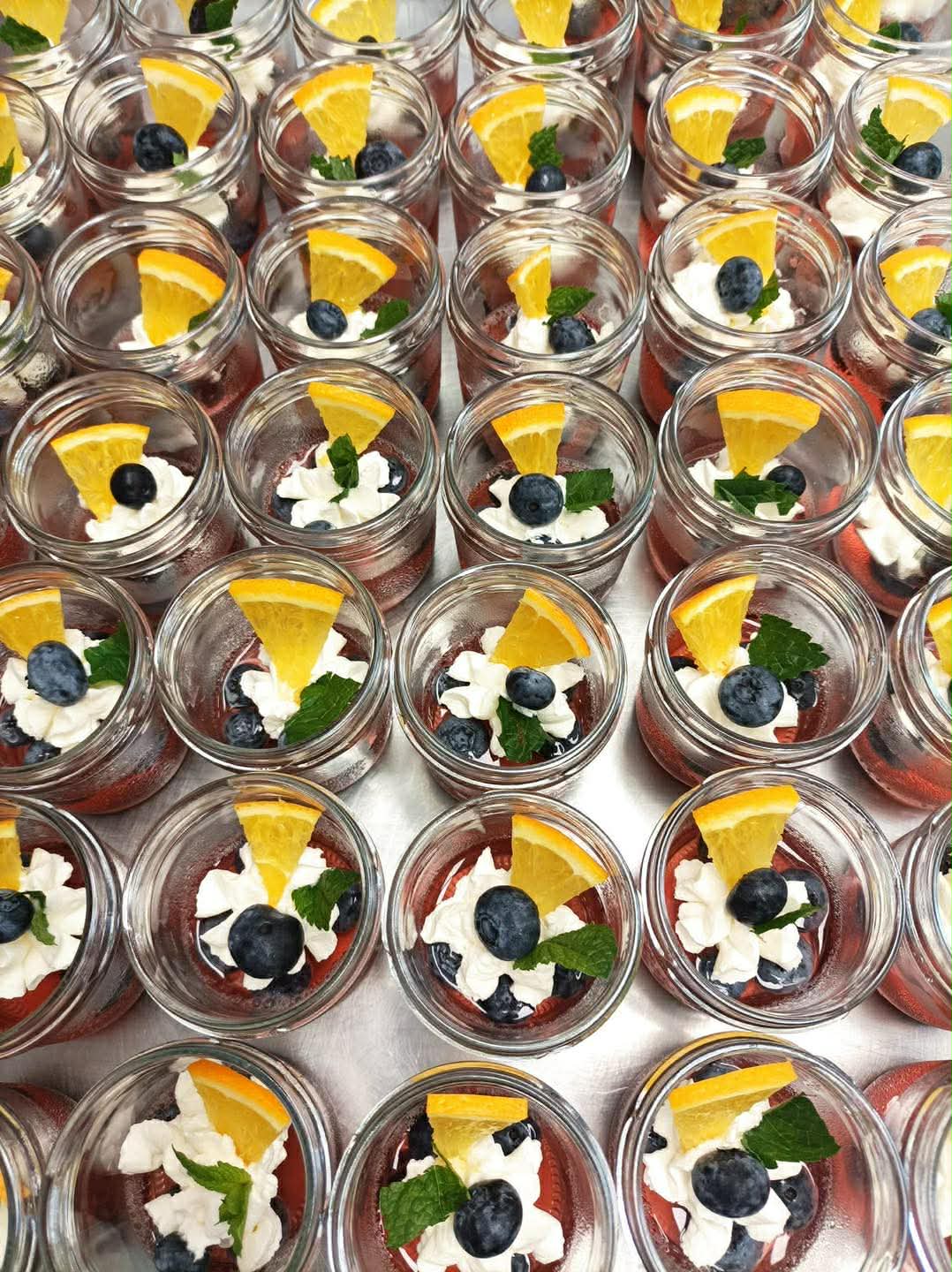 Małe słoiczki z deserem z bitą śmietaną, borówkami i plasterkami pomarańczy.