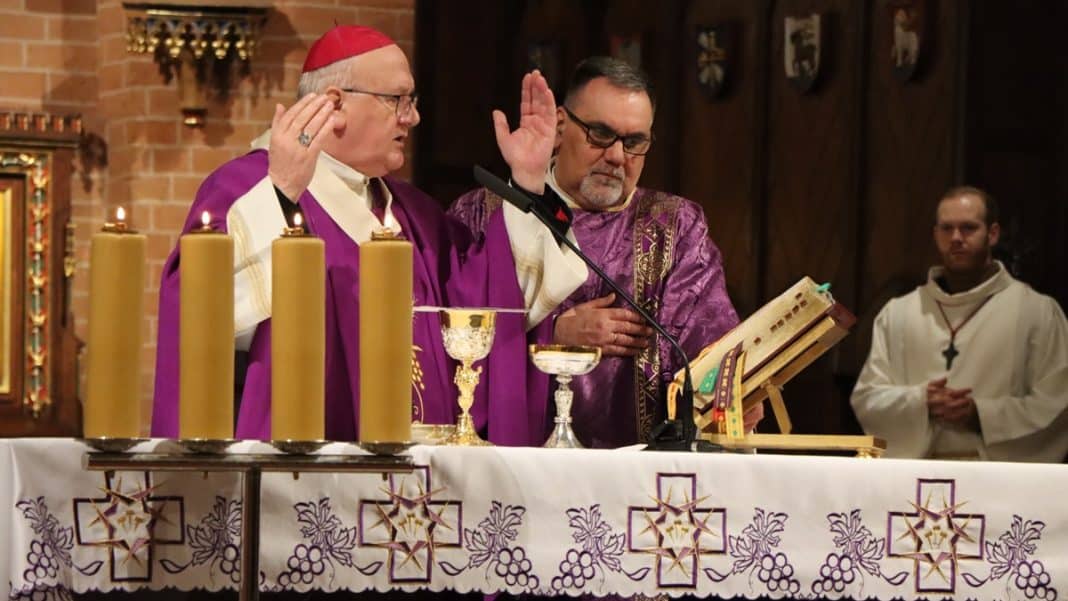 Ksiądz i biskup podczas mszy w konkatedrze św. Jakuba w Olsztynie, przy ołtarzu z świecami i kielichami.
