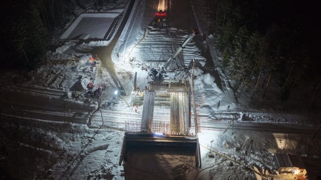 Widok z powietrza na plac budowy w nocy, z ciężkim sprzętem i oświetleniem, w śnieżnym otoczeniu.