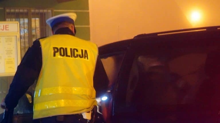 Policjant w kamizelce z napisem 'Policja' zatrzymuje samoch&oacute;d na parkingu w Ełku.