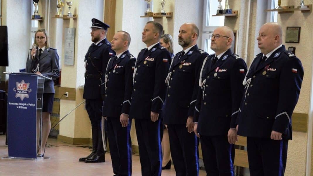 Policjanci w mundurach na konferencji w pomieszczeniu z trofeami na ścianie.