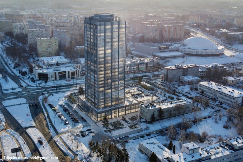 Widok na wysoką wieżę i otaczające ją budynki w zimowej scenerii miasta, z pokrytymi śniegiem ulicami i lasami.