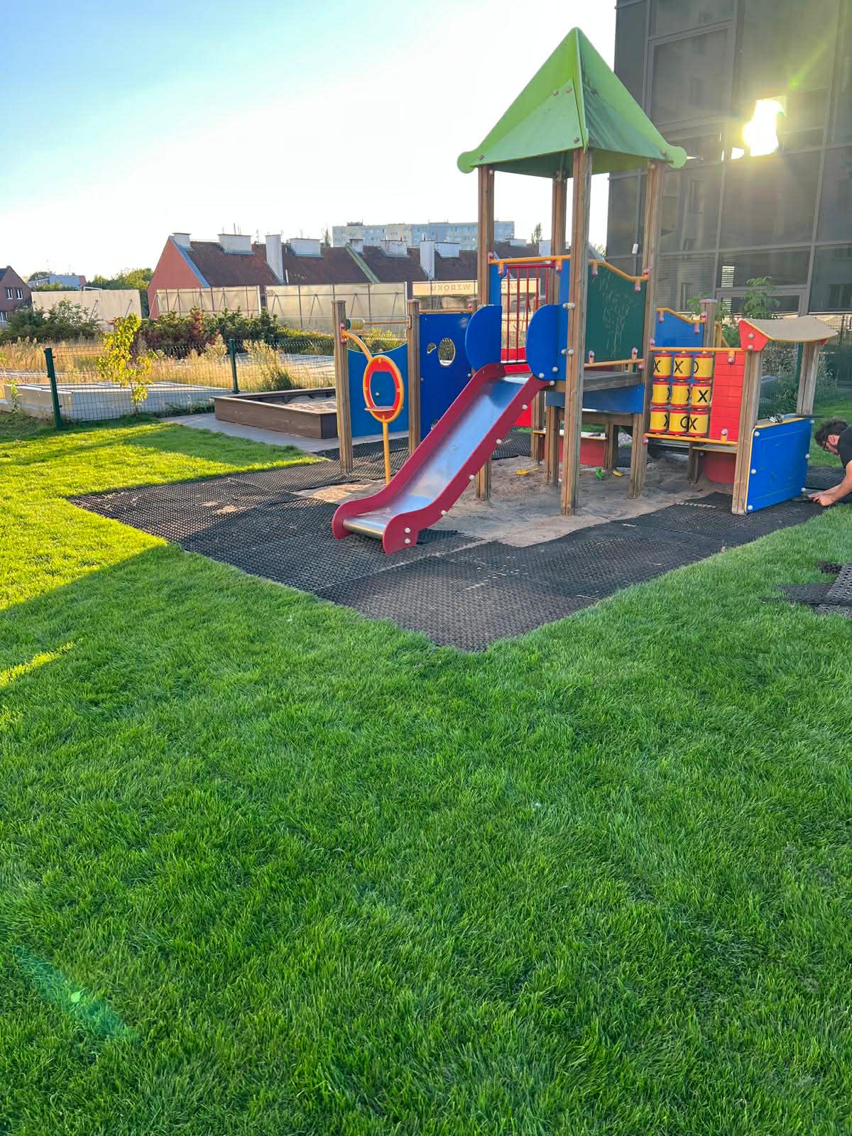 Kolorowy plac zabaw na zewnątrz, zjeżdżalnia i konstrukcje dla dzieci, otoczony zieloną trawą.