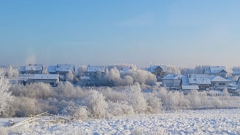 Zamrożony krajobraz z domami i drzewami pokrytymi śniegiem pod błękitnym niebem.