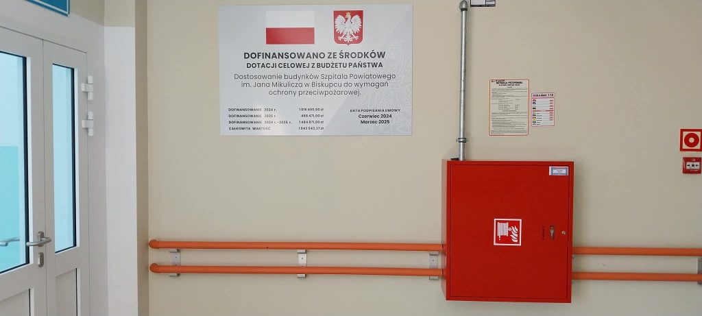 Tablica informacyjna na ścianie szpitala z informacją o dofinansowaniach z budżetu państwa.