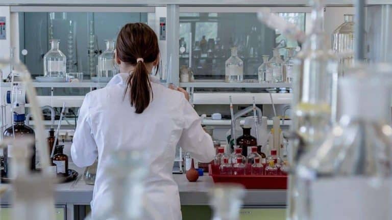 Laborantka pracująca w laboratorium, widok od tyłu, otoczenie prob&oacute;wek i sprzętu chemicznego.