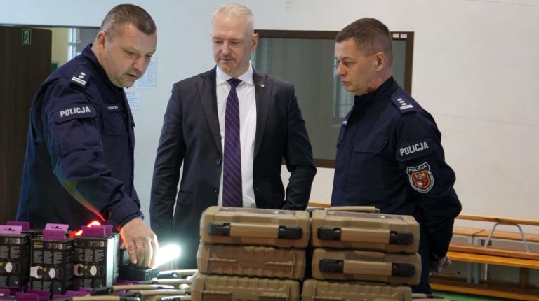 Policjanci i urzędnik przy stoisku z nowoczesnym sprzętem i szkoleniami.