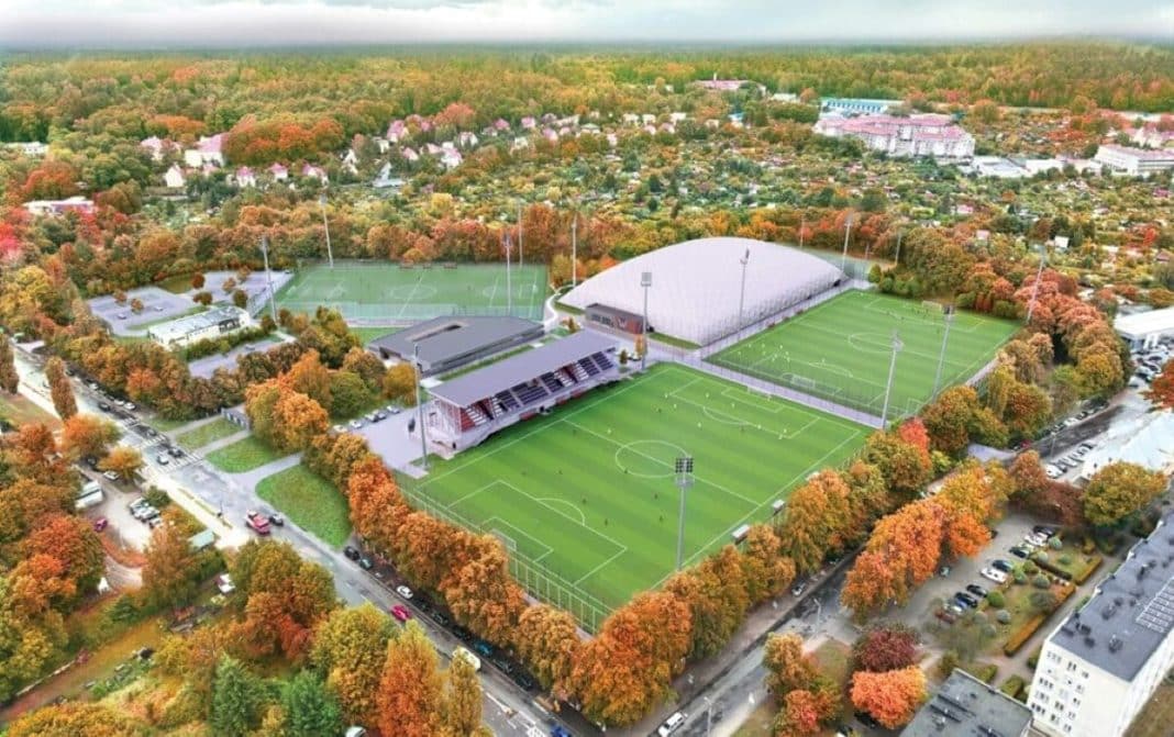 Widok na kompleks boisk sportowych otoczony drzewami o jesiennych barwach w Olsztynie.