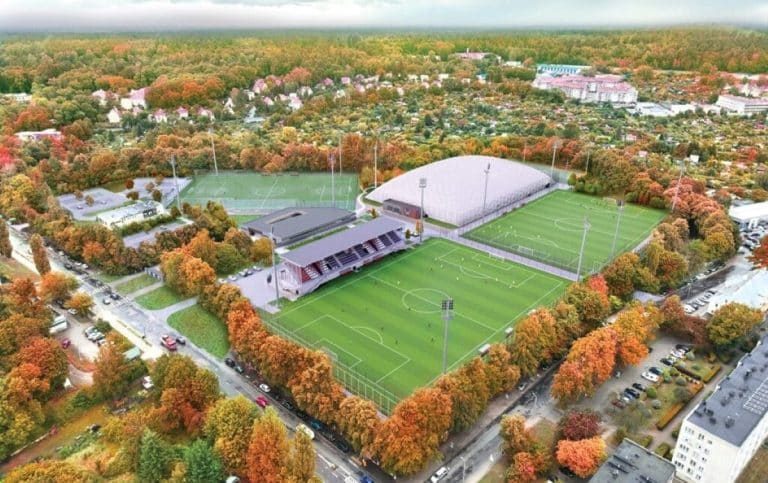 Widok na kompleks boisk sportowych otoczony drzewami o jesiennych barwach w Olsztynie.