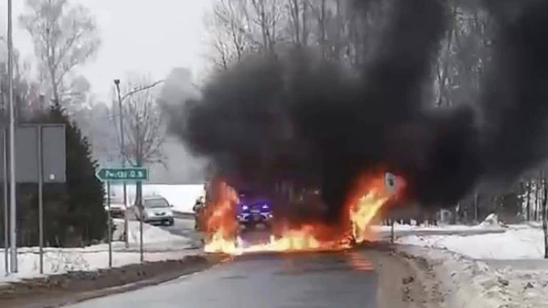 Pożar ciągnika na skrzyżowaniu, kłęby czarnego dymu i płomienie na drodze w zimowej scenerii.