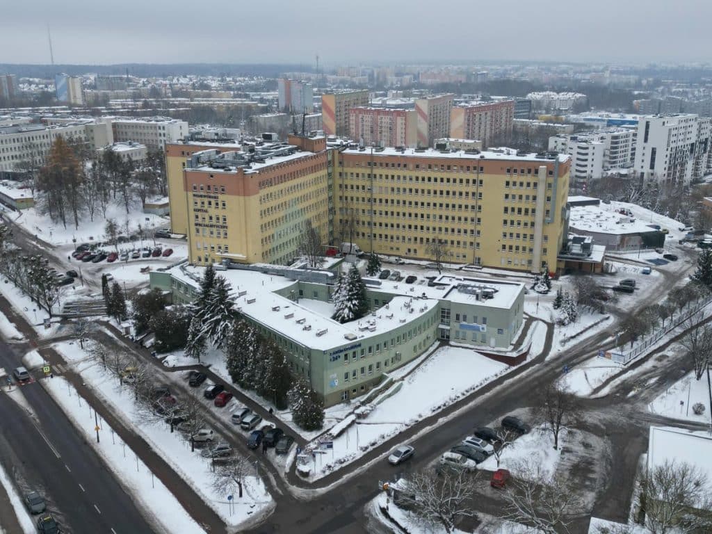 Widok na szpital w zimowej scenerii z zaśnieżonymi budynkami i ulicami.