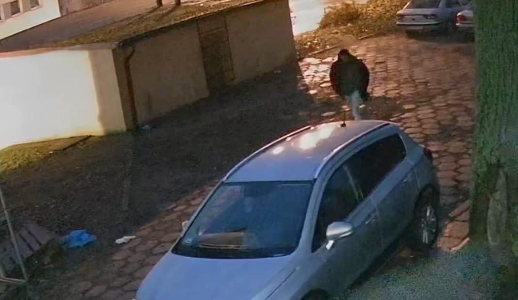 Mężczyzna na parkingu na Zatorzu, poruszający się między samochodami, zatrzymuje się przy jednym z nich.