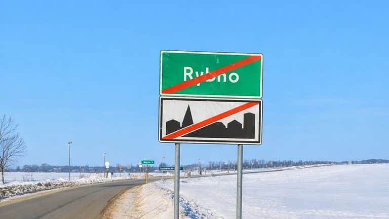 Zimowa droga z tablicą końca miasta Rybno i widokiem na pola i niebo.