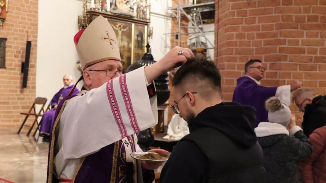 Ksiądz posypuje popiołem wiernego podczas obrzędu w kościele.