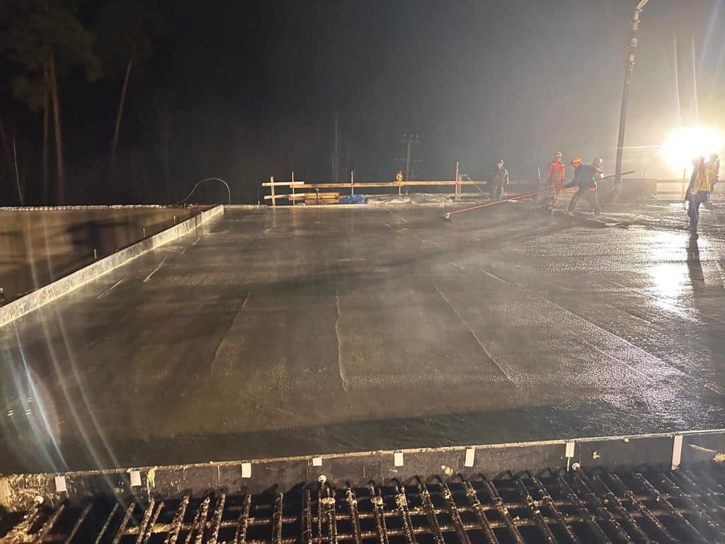 Prace budowlane na nowym odcinku drogi w nocy, z widocznym ciężkim sprzętem i robotnikami.